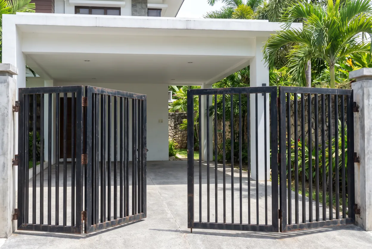 Black steel folding gate with its hinged leaves folded open at a carport